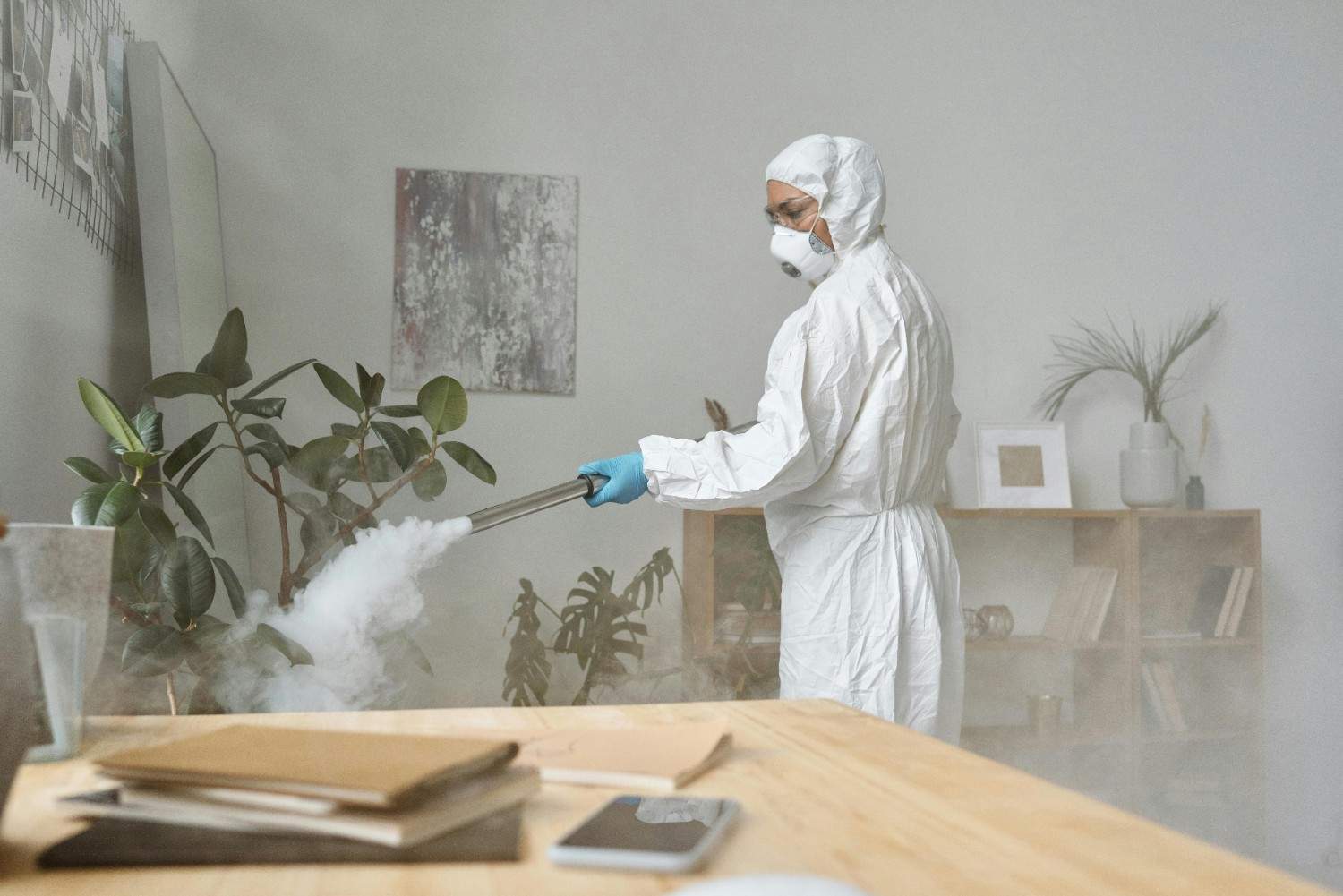 Pest control worker in protective suit spraying indoors
