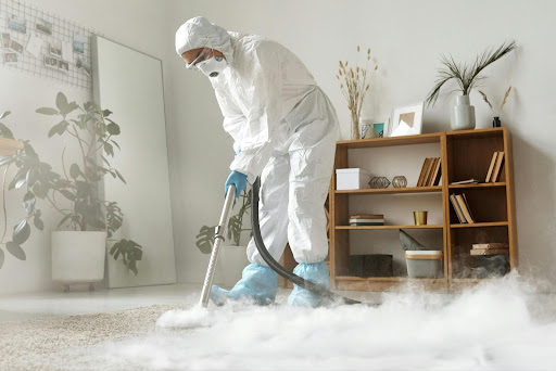 Professional disinfection service technician in a protective suit fogging and disinfecting a room's carpet