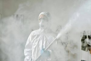 Pest control specialist in protective gear performing indoor chemical fogging for disinfection