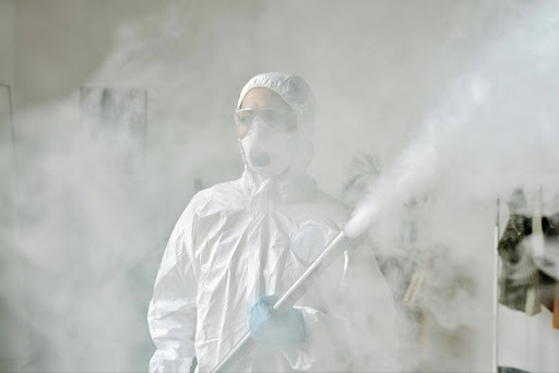 Pest control specialist in protective gear performing indoor chemical fogging for disinfection