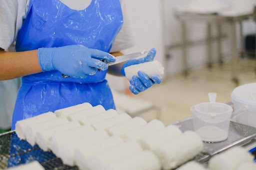 Cheesemaker in blue gloves shaping a small log of fresh white cheese